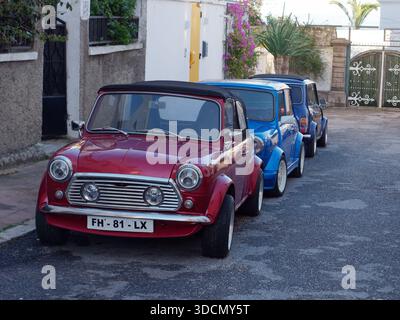 Tre Mini classiche parcheggiate su una strada a Tangeri, una rossa e due blu di sfumature diverse. Marocco. Dic 2025 Foto Stock