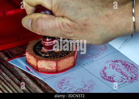 Una mano preme un timbro rosso in un libro di pellegrinaggio Kumano Kodo (nōkyōcho) alla scatola dei timbri del Kumano Hongū Taisha, Tanabe, Prefettura di Wakayama, Giappone. Foto Stock