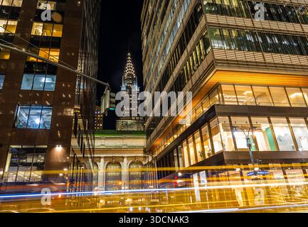 Vista notturna del Chrysler Building tra torri di vetro con percorsi a luci gialle nel centro di Manhattan; ideale per viaggi, affari, finanza Foto Stock