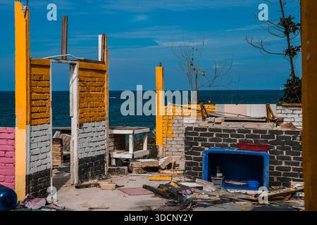resti sbriciolati di una struttura in mattoni demolita contro un oceano blu profondo e un cielo luminoso. Foto Stock