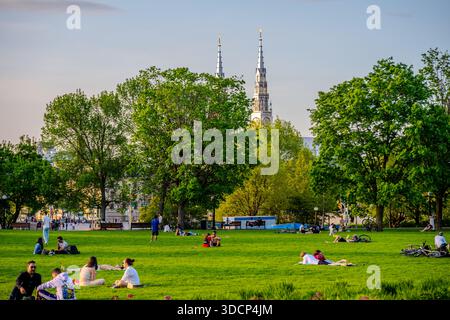 Gruppi di persone siedono e sdraiati sull'erba in un parco verde mentre alte guglie della chiesa si innalzano sopra gli alberi di Ottawa, Canada. Ottawa, Canada - 16 maggio 2024 Foto Stock