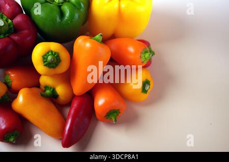 un vivace assortimento di peperoni rossi, verdi, gialli e arancioni e mini peperoni dolci disposti su una superficie liscia e bianchissima che ne esalta la qualità Foto Stock