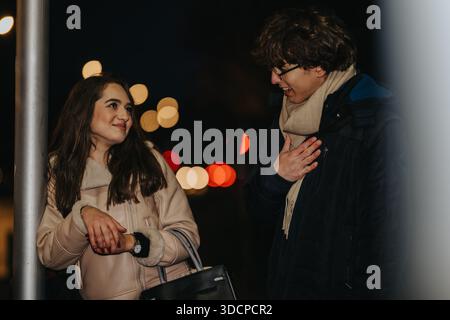 Due adolescenti condividono un momento di amicizia in una strada della città di notte, sorridendo e parlando Foto Stock