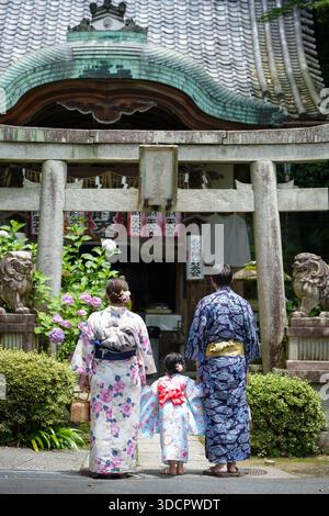 Ｆamily indossa yukata in piedi di fronte al tradizionale cancello torii in pietra con ortensie. Kyoto, Giappone. Foto Stock