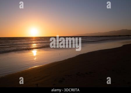 Il tramonto dorato si riflette sulle calme onde dell'oceano sulla costa Foto Stock