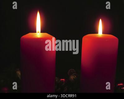 Due candele rosse accese creano un'atmosfera calma e contemplativa al buio, corona dell'Avvento con due candele accese, luce, luci e decorazioni natalizie Foto Stock