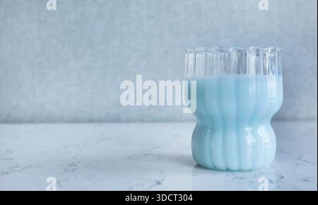 Fotografia dal design minimalista con vetro a coste testurizzato riempito con una bevanda color blu pastello cremosa. La bevanda, che assomiglia al latte di mirtillo, Foto Stock