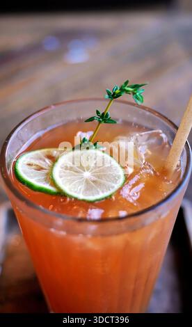 Un rinfrescante bicchiere di tè al limone ghiacciato o di tè alla pesca servito su un tavolo di legno in un bar. La bevanda color ambra è guarnita con lim verde fresco Foto Stock