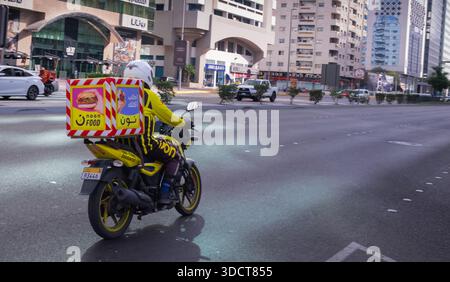 L'autista di motociclette consegna il cibo. Corriere sullo scooter che consegna il cibo a Dubai Road, facendosi strada attraverso le strade trafficate. Servizio di consegna ma Foto Stock