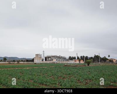 Sottostazione elettrica in un ambiente rurale, che fornisce energia attraverso linee di trasmissione ai campi agricoli verdi circostanti sotto un cielo nuvoloso Foto Stock