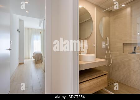 Vista del corridoio luminoso con bagno elegante e camera da letto con finiture in legno e illuminazione soffusa Foto Stock