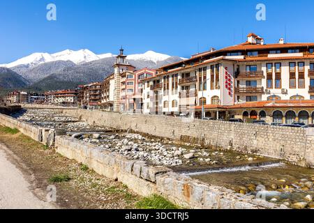 Bansko, Bulgaria - 9 aprile 2025: Fiume Glazne nella città bulgara, case alberghiere e cime innevate dei monti Pirin Foto Stock