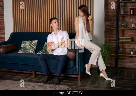 Ritratti coppia elegante e alla moda, litigando e giurando di risentimento e malinteso, seduti su un divano, all'interno di un moderno edificio residenziale interno. Crisi nelle relazioni familiari || modello rilasciato Foto Stock