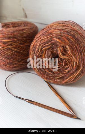Filato marrone caldo con aghi per maglieria in legno su sfondo bianco. Aghi per maglieria e sfere di filato d'arancia. Palla e aghi in filato merino morbido. Foto Stock
