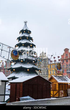 Un albero di Natale spolverato di neve con baule dorate e stella sorge su bancarelle di legno a Wroclaw Rynek, con facciate barocche e rinascimentali e Mini Don Foto Stock