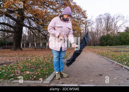 Donna di mezza età che apre un ombrello all'aperto per proteggersi dal maltempo. Vita quotidiana, stile di vita, ambiente urbano. Foto Stock