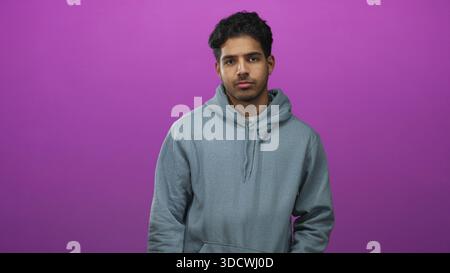 Man in felpa con cappuccio grigia mostra il pollice verso il basso con il pollice visibile ed espressione neutra in studio; rifiuto disapprovazione. Foto Stock