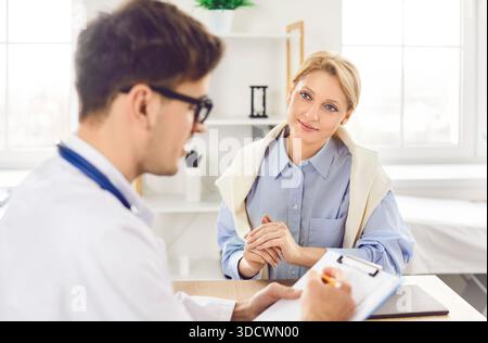 Medico terapeuta maschile che indossa uniforme bianca consultando giovane paziente donna su appuntamento Foto Stock