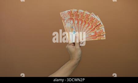 Mano di un uomo caucasico con più pesos filippini su sfondo marrone. Foto Stock