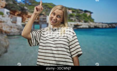 La donna punta il dito verso l'alto in studio indossando una camicia a righe e sorridendo in alto a destra; scoperta dell'ottimismo. Foto Stock