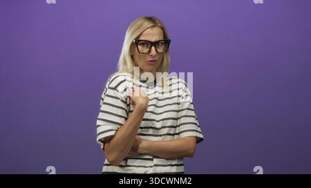 Donna che indossa occhiali oversize e camicia a righe, mano sulla spalla con braccio incrociato e dito puntato, studio; scetticismo. Foto Stock