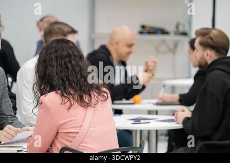 un gruppo di persone siede a tavoli rotondi in una sala luminosa e moderna, discutendo appunti e idee. Foto Stock