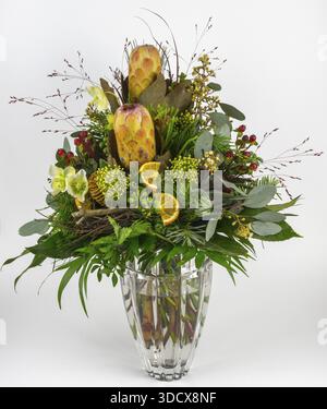 Esotica composizione floreale con protea, rosa di Natale e frutti di bosco in un vaso di vetro, presentato in modo decorativo Foto Stock