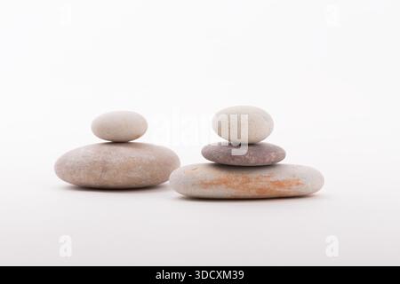 Due cairns di pietre bilanciate su uno sfondo bianco brillante, a dimostrazione di equilibrio, stabilità e calma. Foto Stock