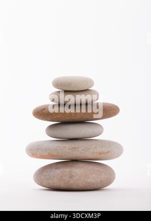 Una pila di pietre lisce disposte ad arte su uno sfondo bianco pulito. Questa composizione evoca un senso di equilibrio, tranquillità e consapevolezza. Foto Stock