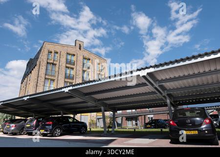Le auto sono parcheggiate sotto una tettoia con pannelli solari in un nuovo condominio. Energia sostenibile e ombra allo stesso tempo Foto Stock