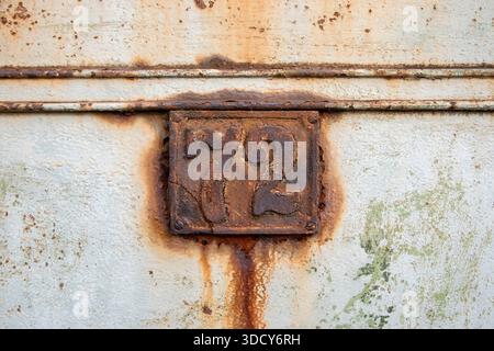 Vecchia targa in ghisa arrugginita sulla porta in metallo resistente agli agenti atmosferici, che simboleggia il tempo, il decadimento e la storia Foto Stock