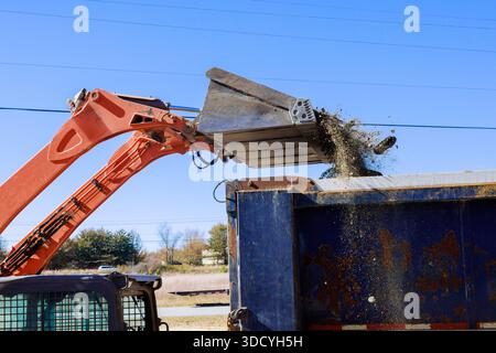 La macchina da braccio con benna grande versa lo sporco di scarto nel contenitore in cantiere. Foto Stock