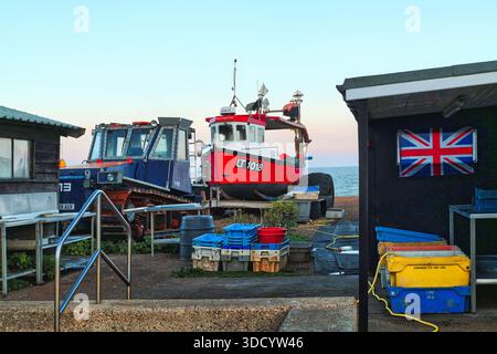 Aldeburgh Beach, Suffolk, Regno Unito - al tramonto, capanne che vendono pesce affumicato sulla spiaggia di ciottoli. Una barca da pesca e un trattore sono tra i negozi Foto Stock