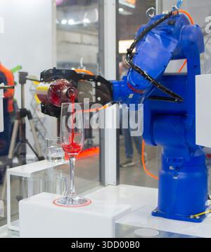 Manipolatori robotici. Robot che versa la bevanda liquida dalla bottiglia al bicchiere. Robot industriale. Mano del braccio del robot. Manipolatori industriali per saldature di vario tipo Foto Stock