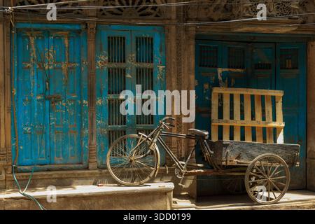 Un risciò è parcheggiato di fronte a una porta blu. La porta è aperta e il riskshaw si appoggia contro di essa. La scena ha un'atmosfera nostalgica e pittoresca Foto Stock