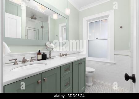 Un elegante bagno con doppio lavandino verde e pareti con ripiano in marmo, pavimento in piastrelle di marmo e lampade a sospensione in vetro. Foto Stock