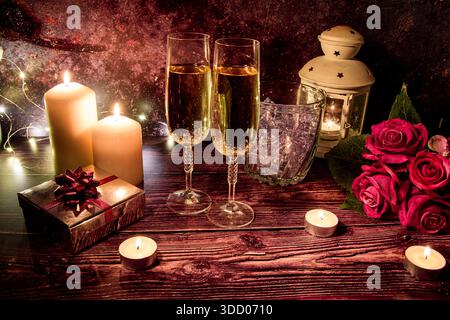 Festa di San Valentino con bicchieri da champagne, secchiello del ghiaccio, candele, rose e confezione regalo su un tavolo rustico in legno. Foto Stock