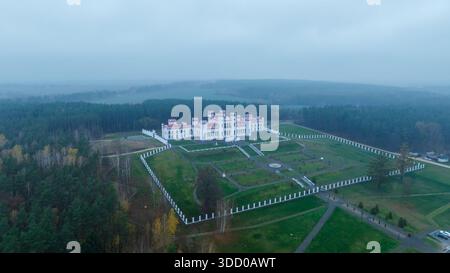 La vista aerea del Palazzo di Kosava nella Bielorussia occidentale mostra facciate neogotiche bianche con torri dal tetto rosso all'interno di un parco rettangolare colonnato, incastonato da mis Foto Stock