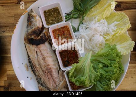 Un vibrante piatto Thai miang pla con pesce alla griglia, spaghetti di riso, erbe fresche, verdure a foglia verde e salse assortite, splendidamente disposte su una Foto Stock