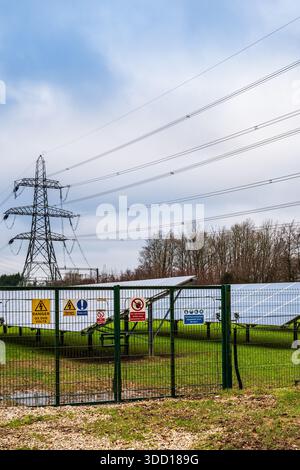 Recinzione di sicurezza Solar Farm con segnali di allarme per alta tensione e piloni - infrastruttura per le energie rinnovabili. Dorset, Inghilterra, Regno Unito Foto Stock