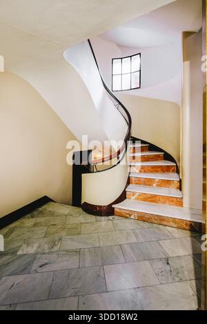 Elegante scala a chiocciola in marmo con corrimano in legno e una piccola finestra all'interno di un edificio storico a Barcellona Foto Stock