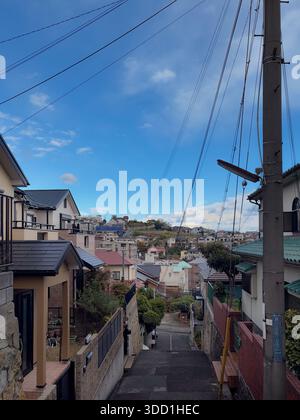 Kobe, Prefettura di Hyogo, Giappone. Stretta strada residenziale su una collina con cavi sospesi, palo e case di quartiere. Foto Stock