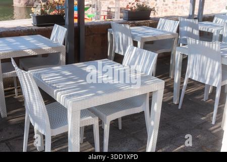 Minimalista allestimento da caffè all'aperto con tavoli bianchi puliti e un design semplice e moderno. La luce soffusa del giorno crea un'atmosfera luminosa e ariosa, ideale per lo stile di vita Foto Stock