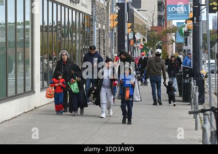 Toronto, ON, Canada - 25 ottobre 2025: Famiglie e bambini in costume camminano su un marciapiede affollato di Toronto, celebrando Halloween e collezionando circa Foto Stock