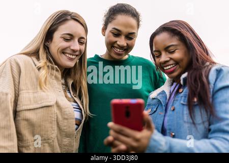 Diverse donne e amiche ridono guardando contenuti sullo smartphone Foto Stock