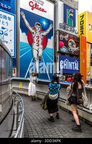 Tre donne fotografano il cartellone Glico sul Canale Dotonbori di Osaka, Giappone. Il famoso Glico Man originariamente pubblicizzava un Energy bar contenente ingredienti di ostriche. Osaka, Prefettura di Osaka, Giappone Foto Stock