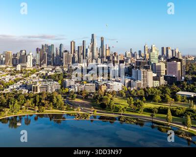 Una vista aerea cattura il moderno paesaggio urbano di Melbourne con numerosi grattacieli, che si riflettono pacificamente nel lago Albert Park, con diverse mongolfiere Foto Stock