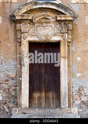 Arcata in pietra intagliata ornata con porta in legno posta in un muro antico Foto Stock