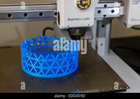 Una stampante 3D Bambu Lab inizia a fabbricare un oggetto cilindrico blu con un reticolo. La testina di stampa è attiva, mostrando i primi passi Foto Stock