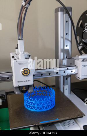 Una stampante 3D Bambu Lab inizia a fabbricare un oggetto cilindrico blu con un reticolo. La testina di stampa è attiva, mostrando i primi passi Foto Stock